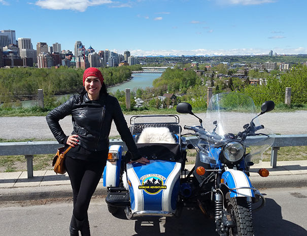 Rocky Mountain Sidecar Adventures Calgary Sightseeing Tour customer posing beside sidecar with Calgary's Bow River behind her