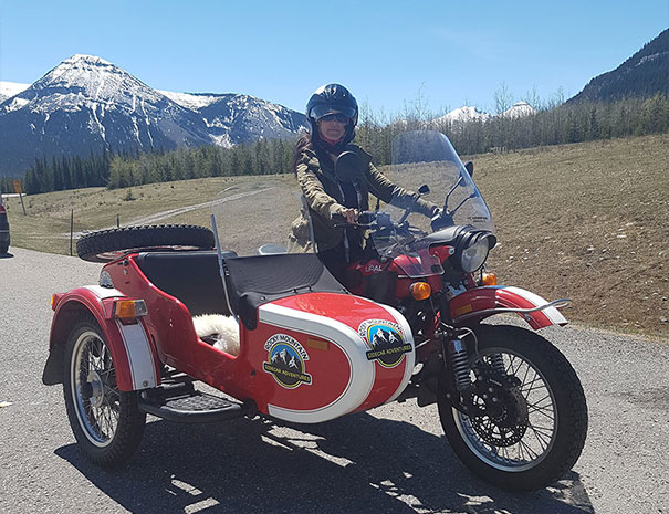 Rocky Mountain Sidecar Adventures customer posing on bike with the beautiful rocky mountains behind her